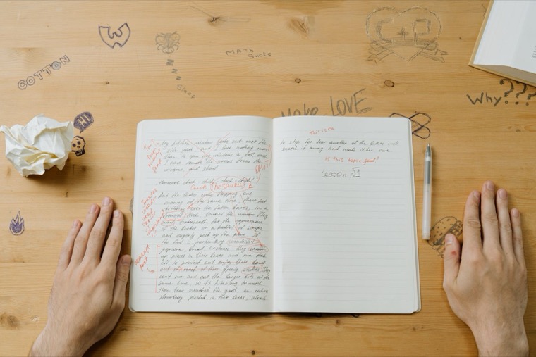 Deux mains posées sur un carnet fermé, sur un bureau clair.